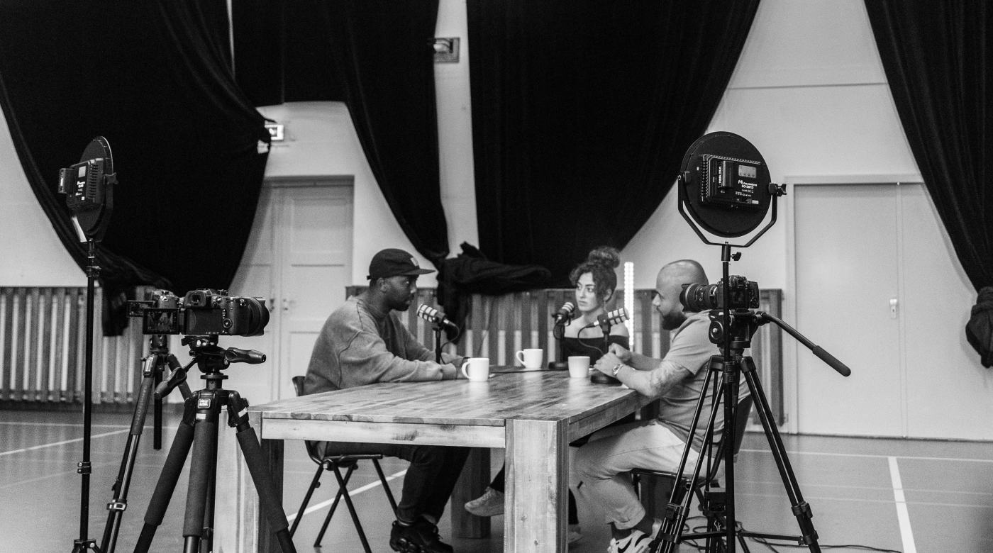Three people recording a podcast around a table with cameras and microphones